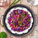 A black bowl of sweet and sour cabbage topped with crispy bacon and sliced scallions.