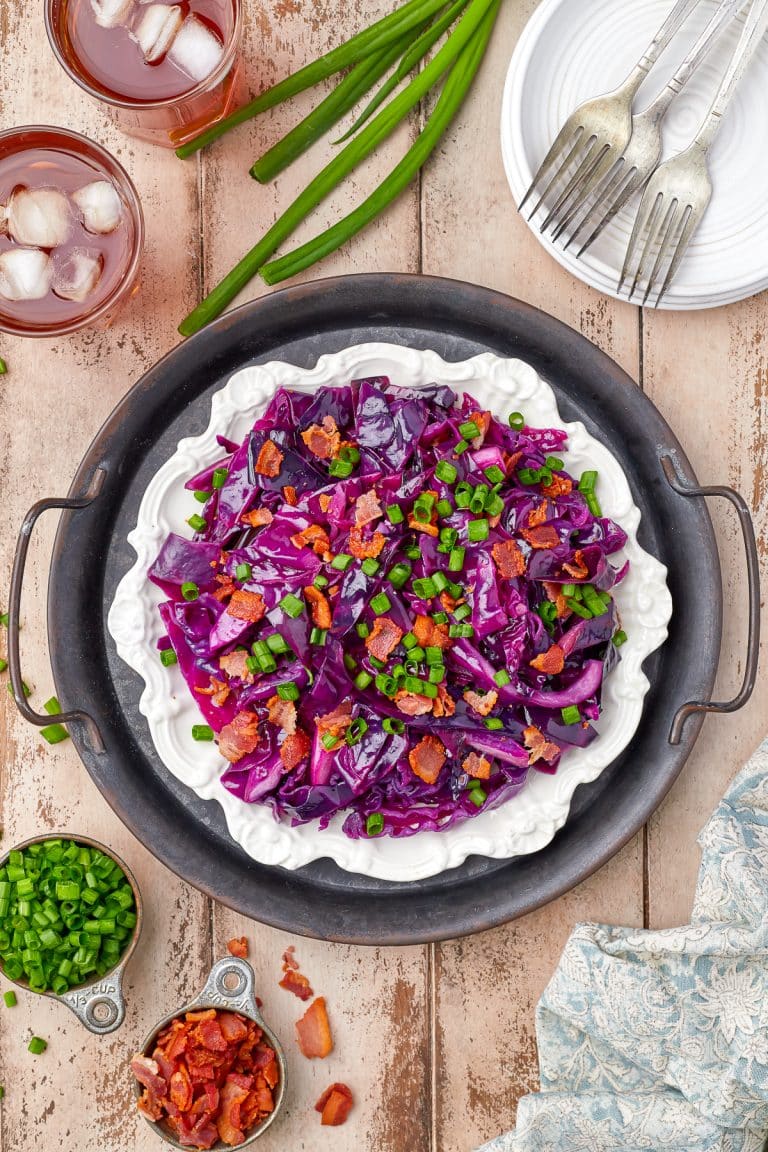 A black bowl of sweet and sour cabbage topped with crispy bacon and sliced scallions.