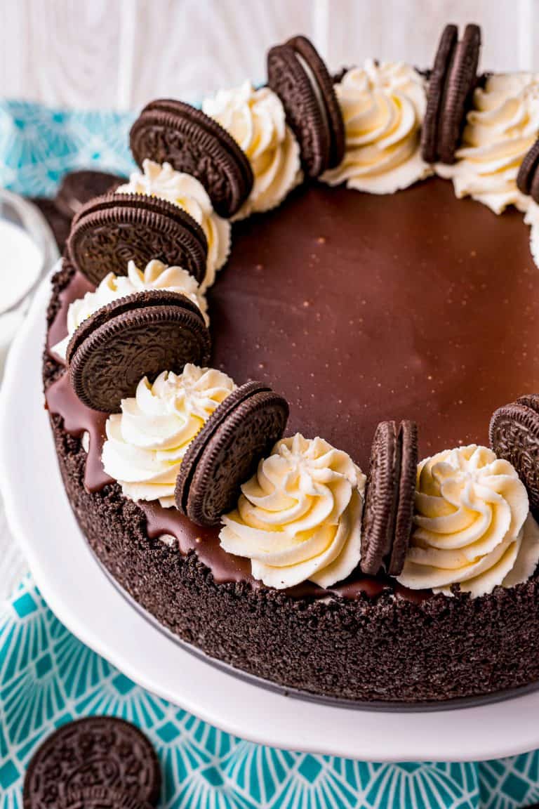 A whole no bake Oreo cheesecake topped with chocolate ganache, whipped cream swirls, and Oreos.