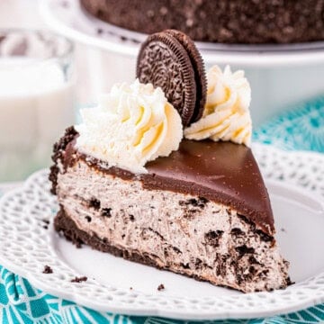 Square image of slice of cheesecake on white plate with whipped cream and Oreo.