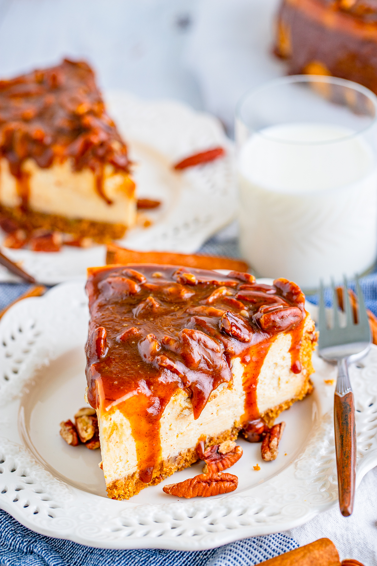 Slice of Pecan Pie Cheesecake on white plate with sauce dripping down sides of cheesecake.
