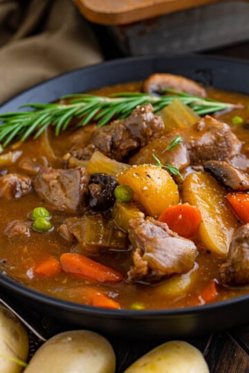 A bowl of hearty venison stew with tender meat, potatoes, carrots, and peas.
