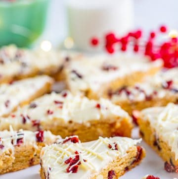 Frosted cranberry bliss bars cut into triangles topped with dried cranberries and white chocolate drizzle.