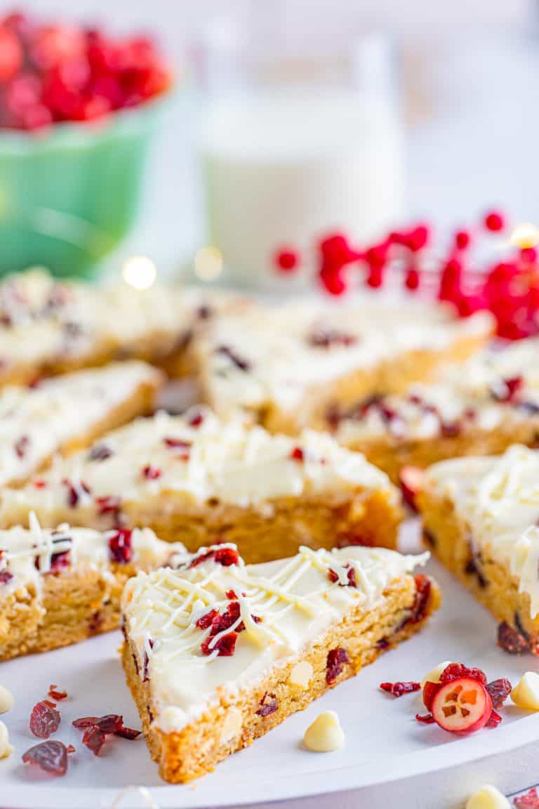 Frosted cranberry bliss bars cut into triangles topped with dried cranberries and white chocolate drizzle.