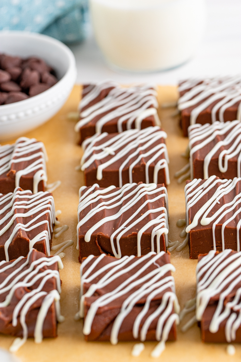 Cut fudge drizzled with white chocolate on brown parchment paper.