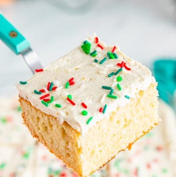A square slice of eggnog cake with white eggnog frosting and Christmas sprinkles lifted on a cake server.
