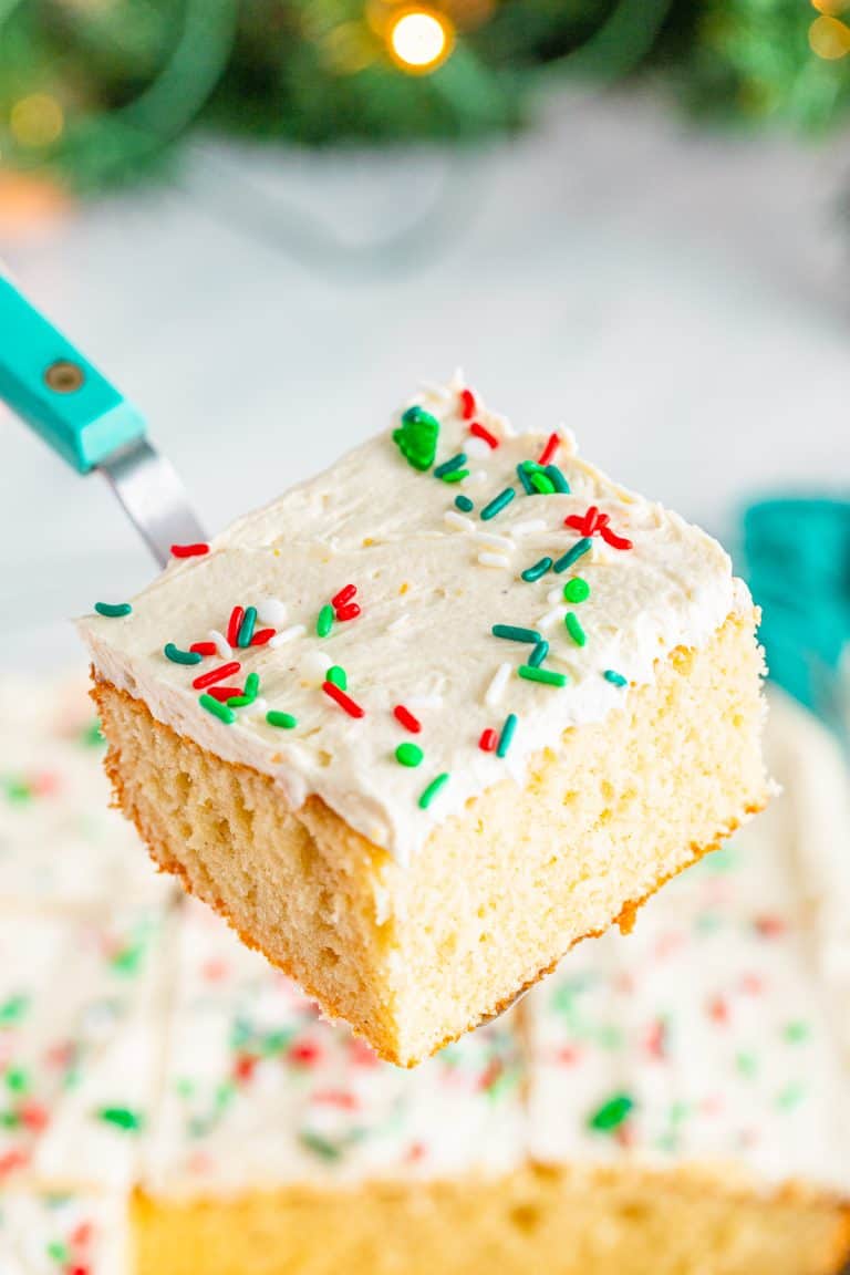 A square slice of eggnog cake with white eggnog frosting and Christmas sprinkles lifted on a cake server.