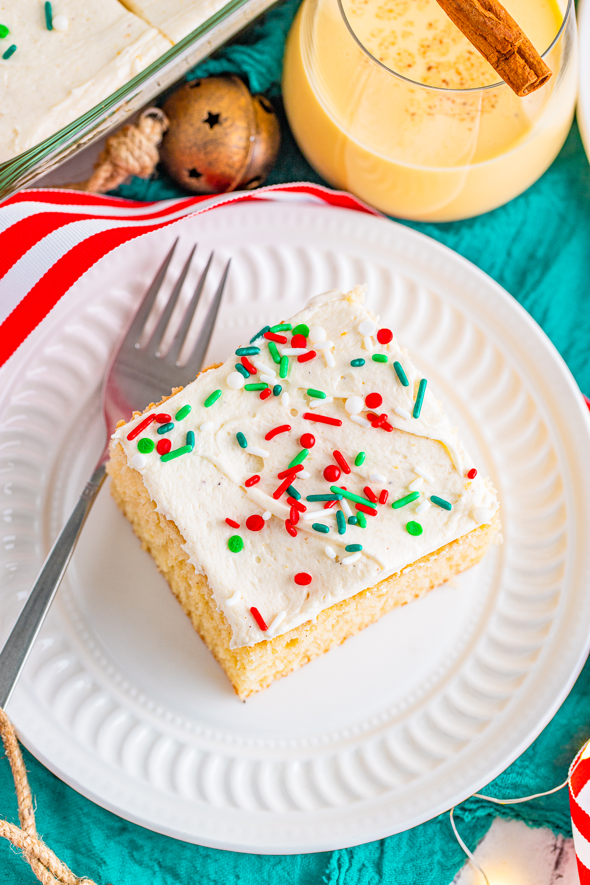 Overhead photo of slice of Eggnog Cake on white plate with fork and glass of Eggnog.