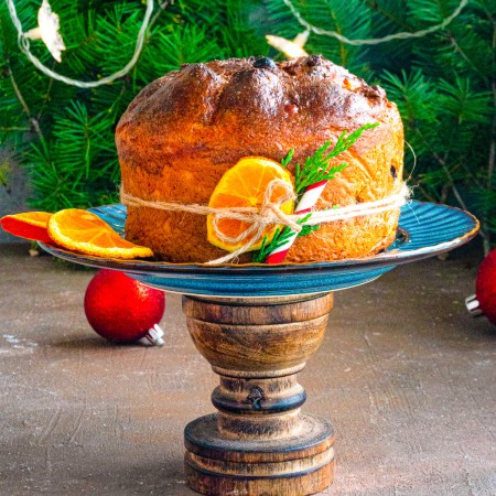 Square image of Panettone on serving plaltter with oranges and tie.