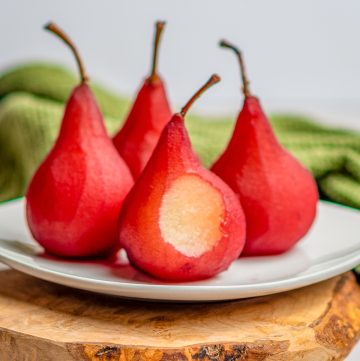 Ruby red wine poached pears standing upright on a white plate.