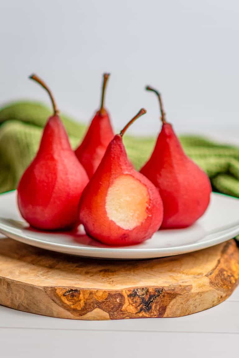 Ruby red wine poached pears standing upright on a white plate.