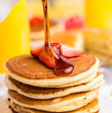 A tall stack of ricotta pancakes with syrup being poured over the top.