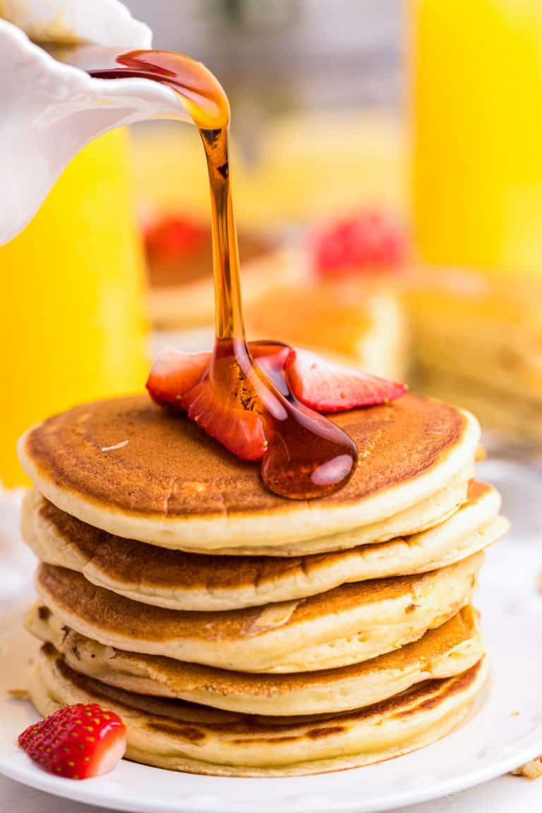 A tall stack of ricotta pancakes with syrup being poured over the top.