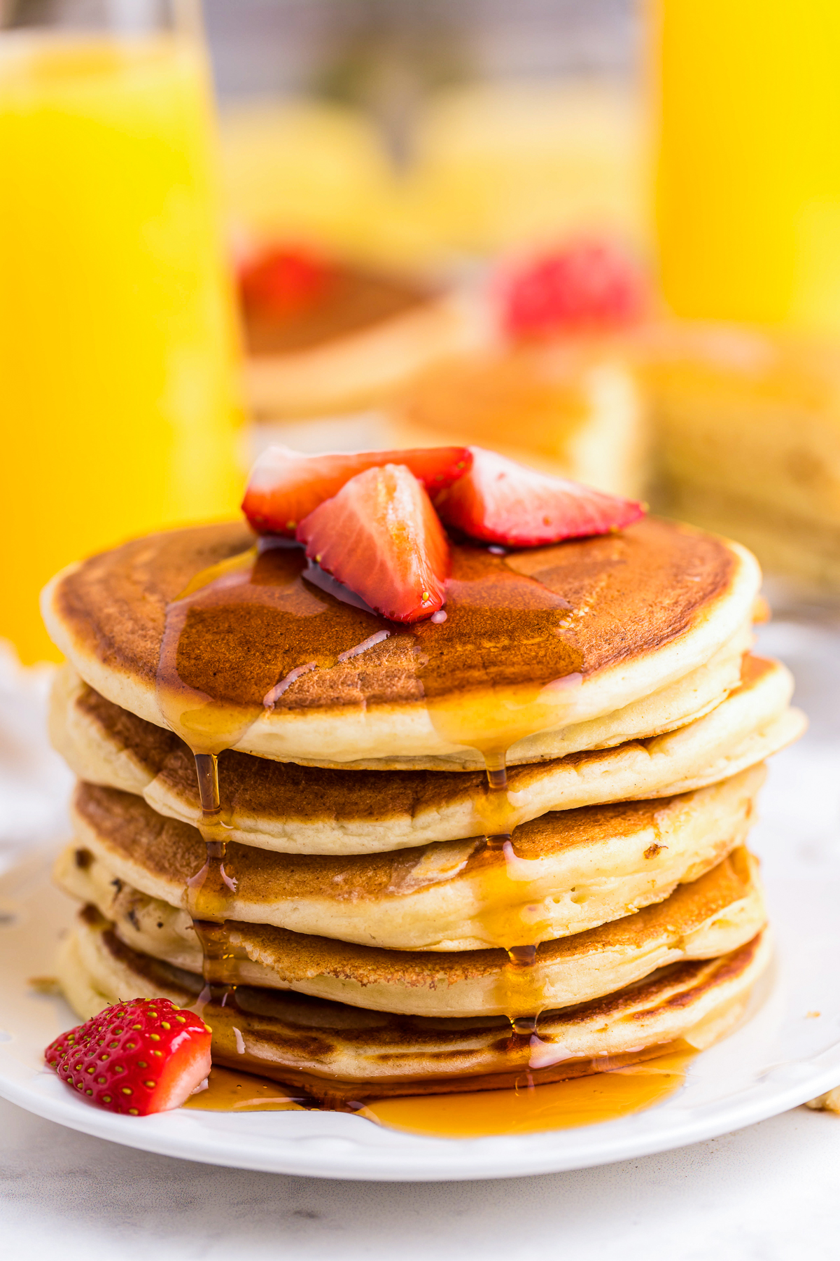 Stack of Ricotta Pancakes topped with syrup and strawberries.