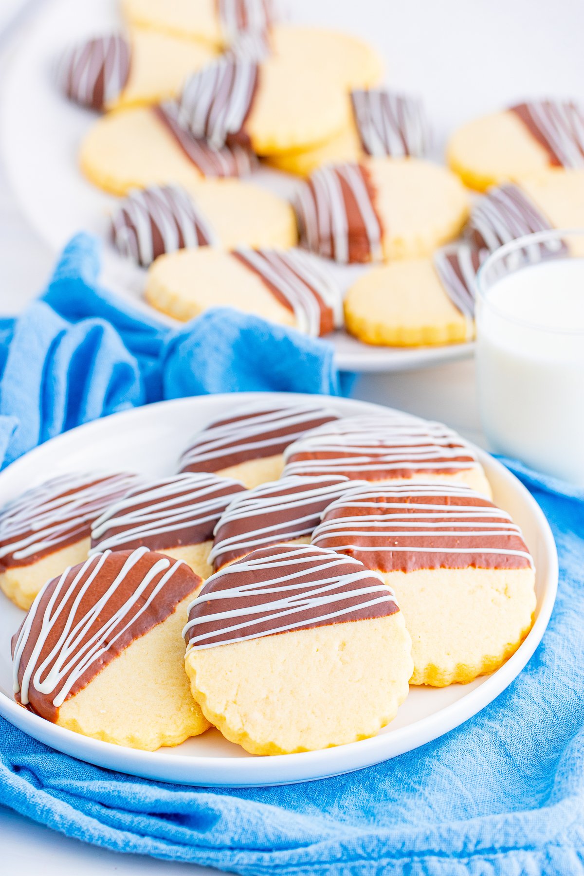 Chocolate Dipped Shortbread Cookies layered on white plates with milk.