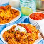Mexican rice casserole on a white plate topped with sour cream and salsa with a fork