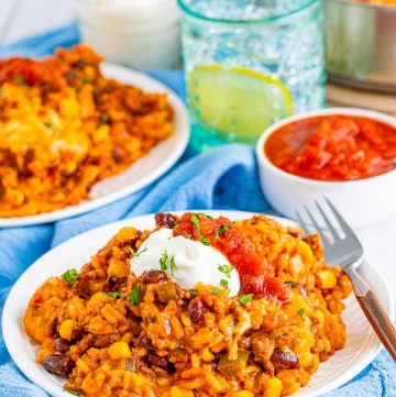 Mexican rice casserole on a white plate topped with sour cream and salsa with a fork