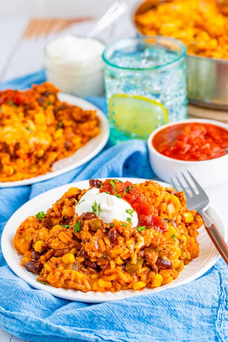 Mexican rice casserole on a white plate topped with sour cream and salsa with a fork