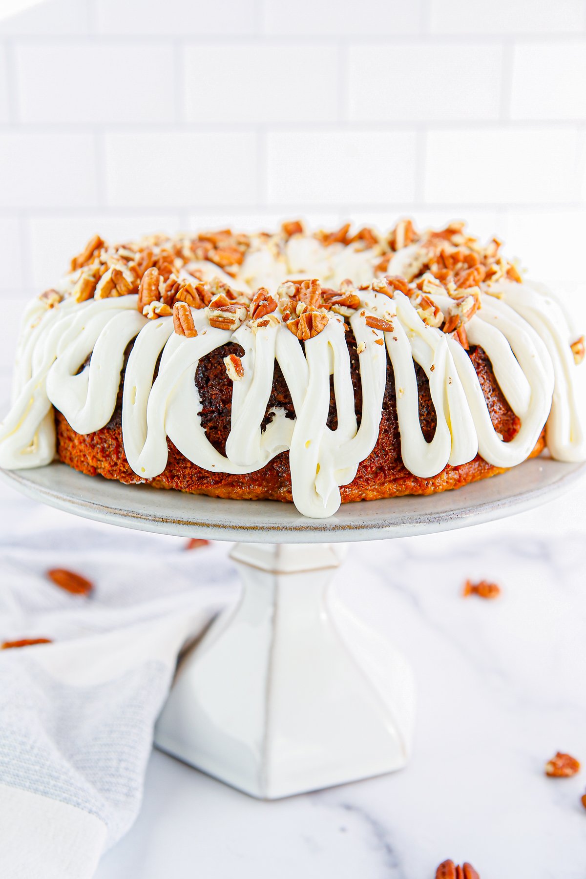 Banana Bundt Cake on cake stand frosted and topped with pecans.