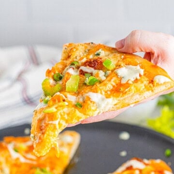Square photo of hand holding up a slice of pizza.