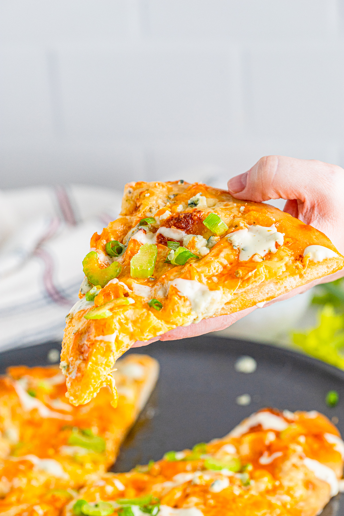 Hand holding up a slice of the Buffalo Chicken Pizza.