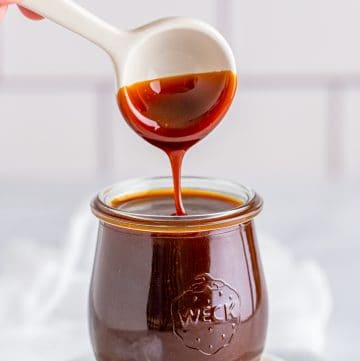 Glossy homemade butterscotch sauce being poured from a ladle into a glass jar.