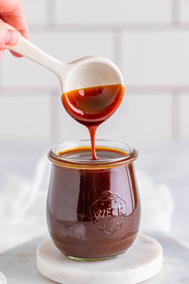 Glossy homemade butterscotch sauce being poured from a ladle into a glass jar.