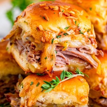 Close up of stacked French Dip Sliders showing melty provolone cheese and tender roast beef on Hawaiian rolls.