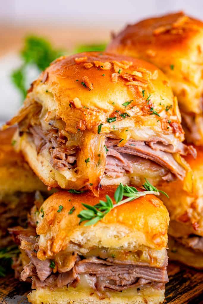 Close up of stacked French Dip Sliders showing melty provolone cheese and tender roast beef on Hawaiian rolls.