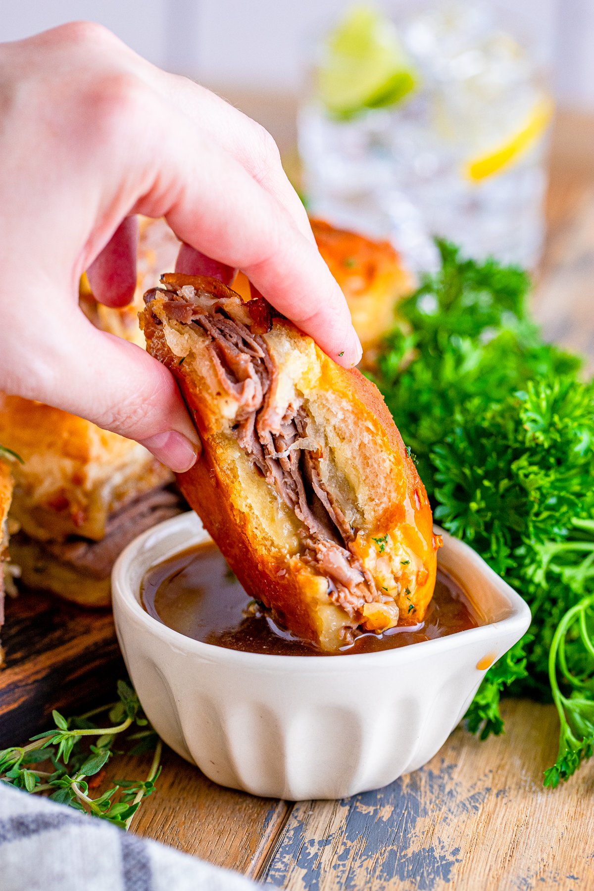 Hand dipping one French Dip Slider into au jus.