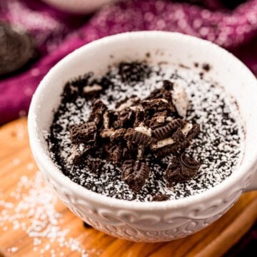 A finished Oreo mug cake topped with crushed Oreos and powdered sugar.