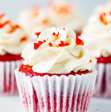 Red Velvet Cupcakes on white board topped with frosting and some cake crumbs.