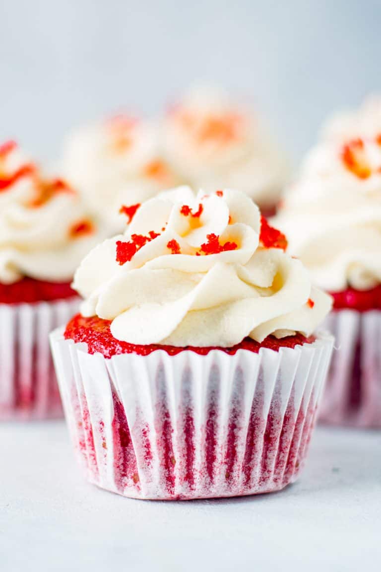 Red Velvet Cupcakes on white board topped with frosting and some cake crumbs.