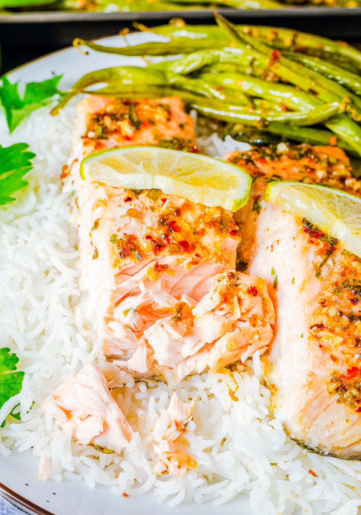 Salmon Sheet Pan Dinner over rice on plate with bite taken out of salmon.