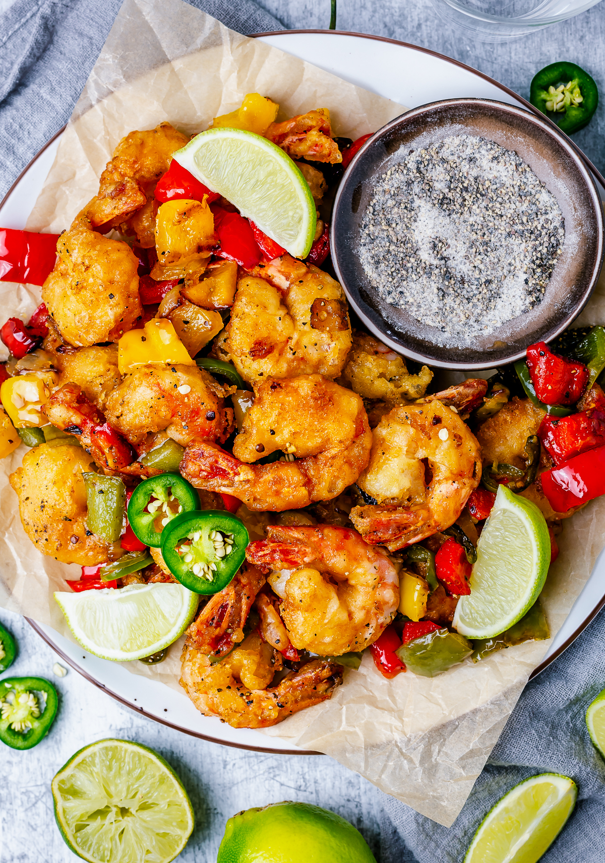 Overhead of finished Salt and Pepper Shrimp on plate with limes and a bowl of salt and pepper.