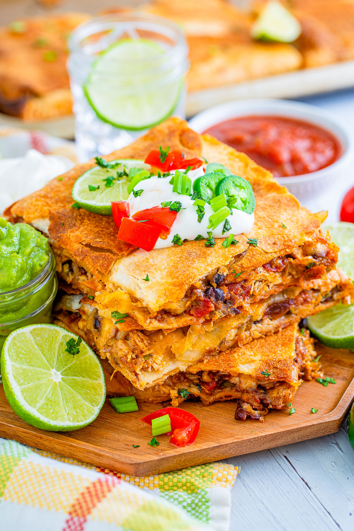 Three cut and stacked Chicken Sheet Pan Quesadilla with toppings and limes next to them.