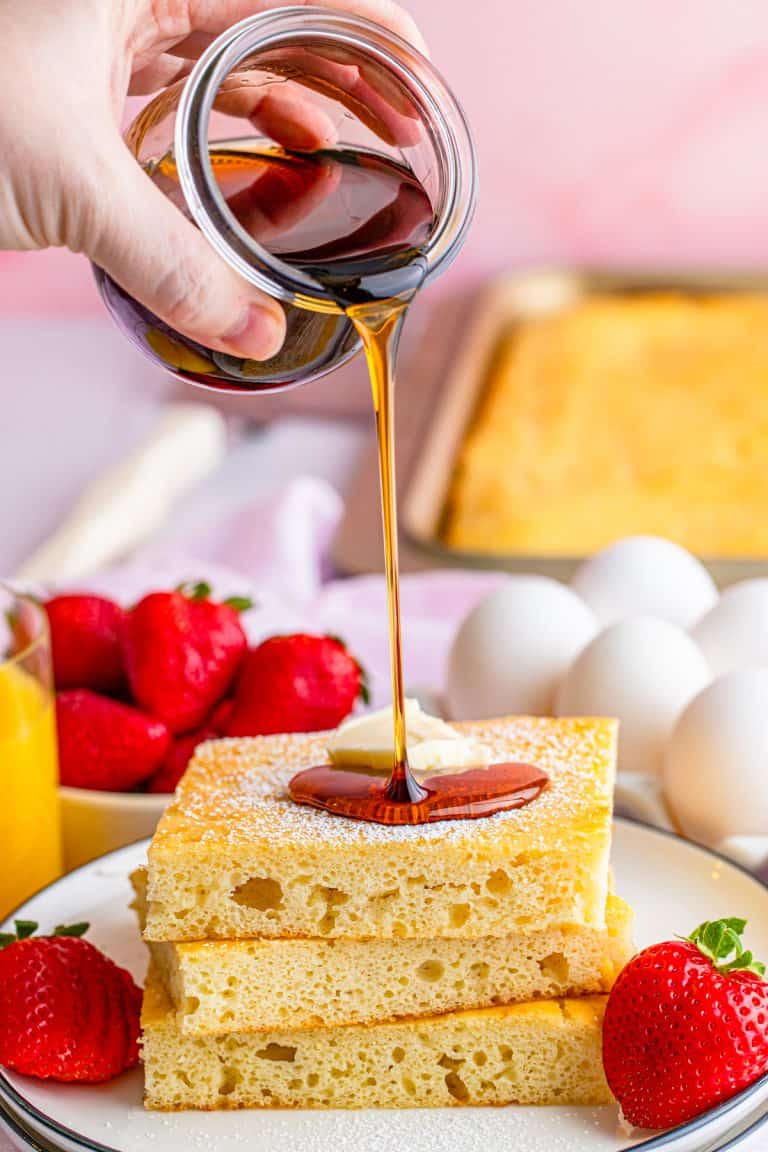 Syrup being poured over stack of cut Sheet Pan Pancakes on plate.