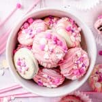 A bowl of chocolate covered Oreos coated in pink and white chocolate with colorful sprinkles.