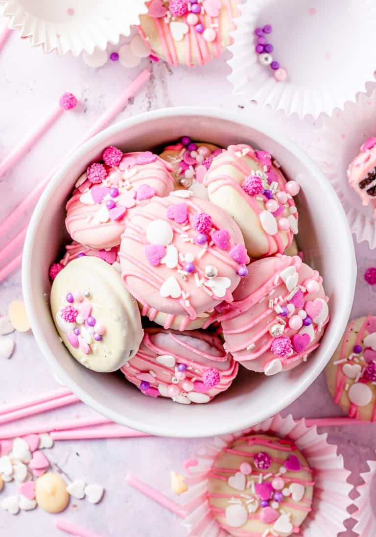 A bowl of chocolate covered Oreos coated in pink and white chocolate with colorful sprinkles.