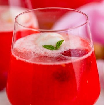 A glass of Sherbet Punch with a scoop of pineapple sherbet floating on top garnished with mint and a raspberry.