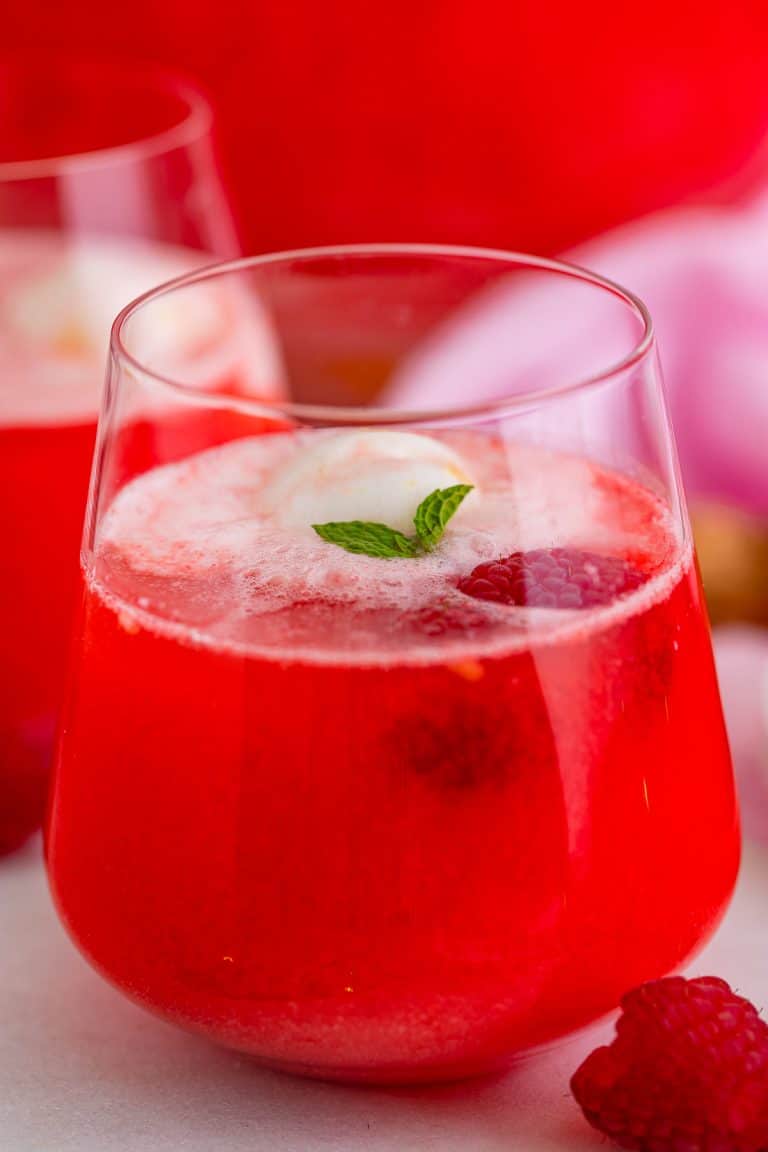 A glass of Sherbet Punch with a scoop of pineapple sherbet floating on top garnished with mint and a raspberry.
