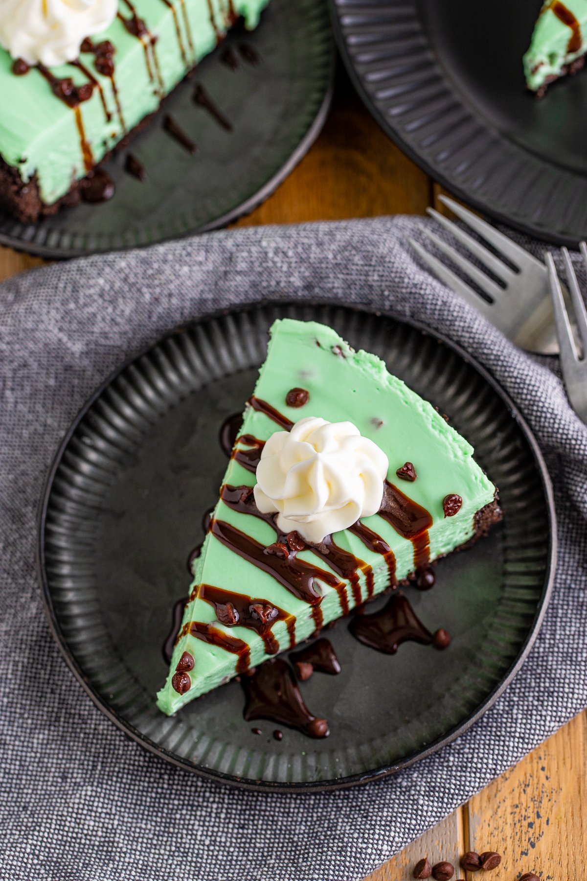 Overhead photo of a slice of No Bake Mint Chocolate Chip Cheesecake with whipped cream, mini chocolate chips and chocolate drizzle.