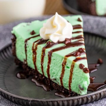 Square image of slice of cheesecake on black plate garnished.
