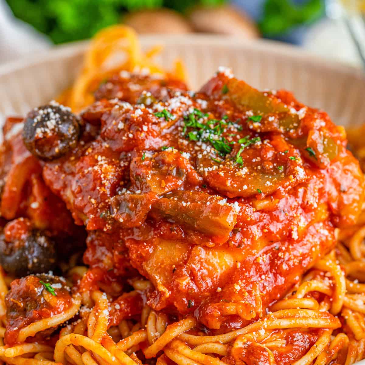 A bowl of chicken cacciatore served over spaghetti and topped with parsley and parmesan.