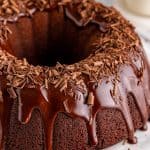 A whole chocolate bundt cake on a stand with glossy chocolate ganache glaze dripping down the ridges.