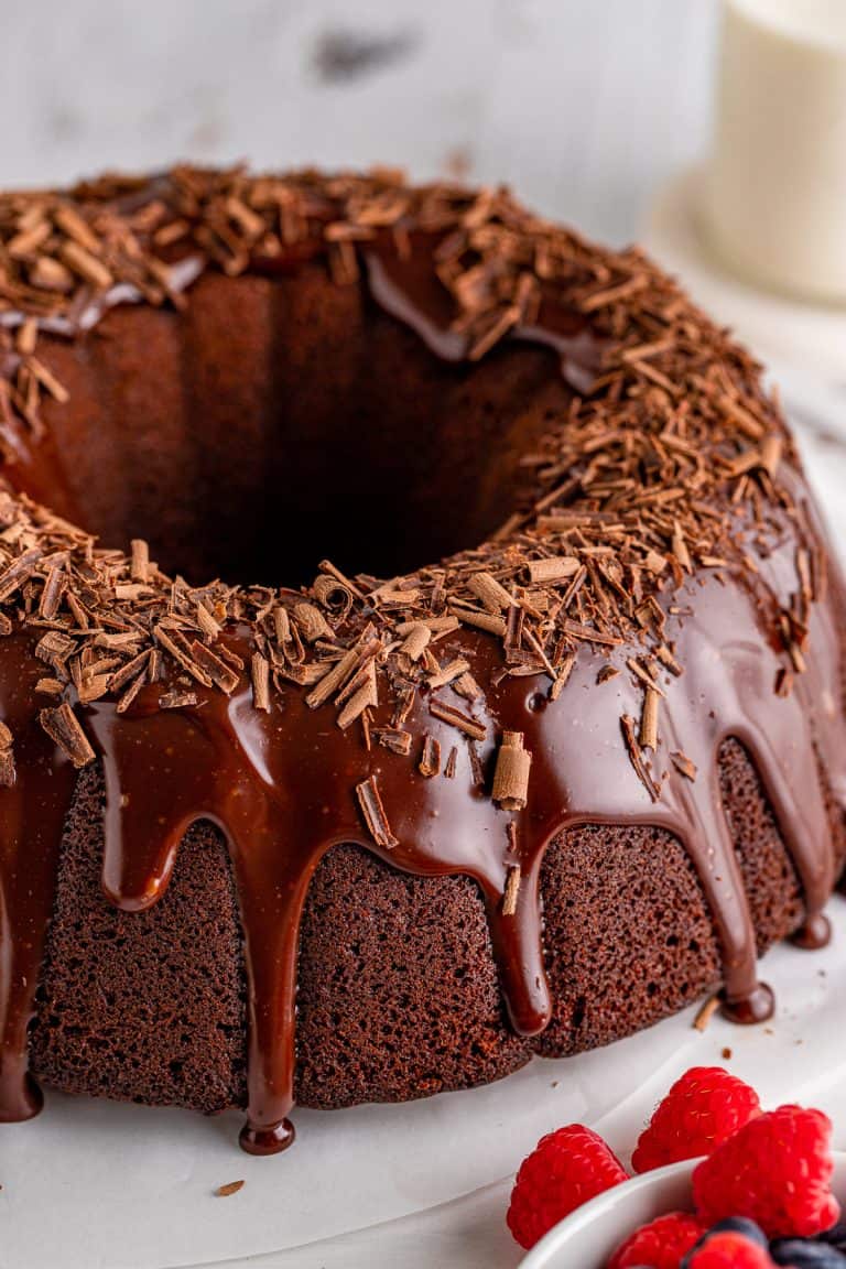 A whole chocolate bundt cake on a stand with glossy chocolate ganache glaze dripping down the ridges.
