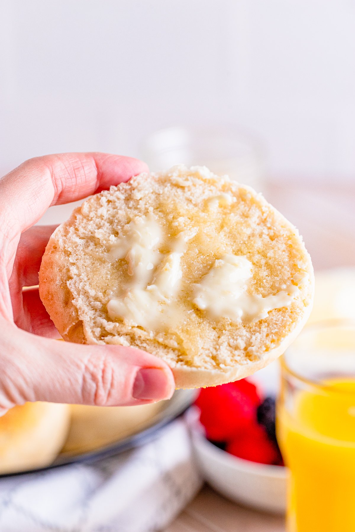 Hand holding up one slice of the English Muffin Recipe showing butter.