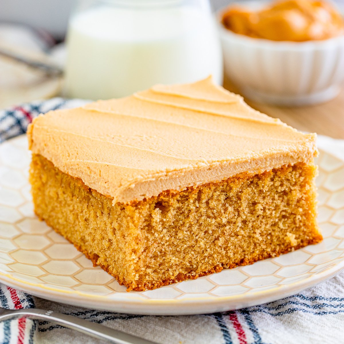 Square image of cake on plate with milk in background.