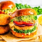 A crispy salmon burger on a brioche bun with lettuce, tomato, and red onion on a wooden board.