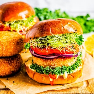 A crispy salmon burger on a brioche bun with lettuce, tomato, and red onion on a wooden board.